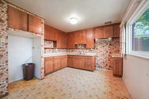 Kitchen featuring a sink, light countertops, ventilation hood, and brown cabinetry