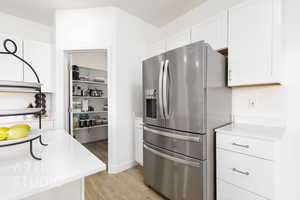 Kitchen featuring white cabinetry, light countertops, light wood finished floors, and stainless steel fridge with ice dispenser