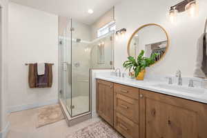 Bathroom with double vanity, baseboards, a shower stall, and a sink
