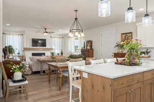 Kitchen featuring a fireplace, a breakfast bar area, light wood-type flooring, light countertops, and a ceiling fan