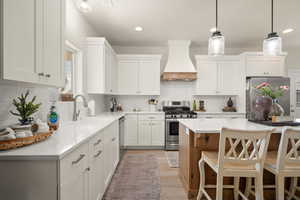 Kitchen featuring a kitchen breakfast bar, appliances with stainless steel finishes, tasteful backsplash, a sink, and premium range hood