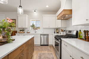 Kitchen featuring light countertops, tasteful backsplash, custom range hood, light wood-style flooring, and appliances with stainless steel finishes