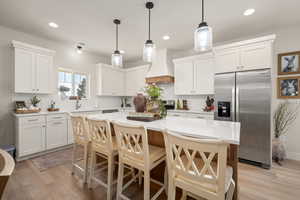 Kitchen featuring light wood-style floors, backsplash, premium range hood, and stainless steel appliances