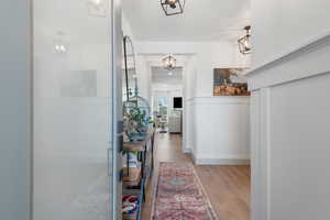Hallway featuring light wood-style floors, a decorative wall, and a wainscoted wall