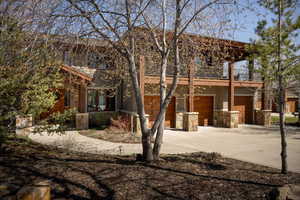 View of front of house featuring driveway, a garage, a balcony, stone siding, and stucco siding