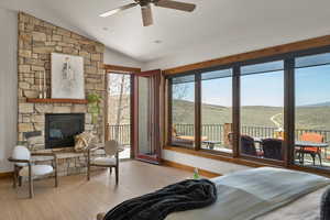 Bedroom featuring a fireplace, access to exterior, baseboards, wood finished floors, and lofted ceiling