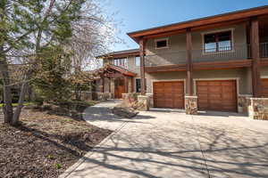 View of front facade with a garage, a balcony, stone siding, stucco siding, and driveway