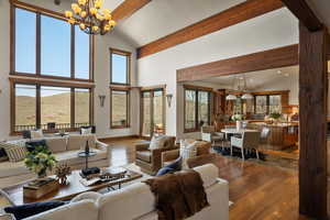 Living room featuring wood finished floors, high vaulted ceiling, beamed ceiling, a notable chandelier, and a wealth of natural light