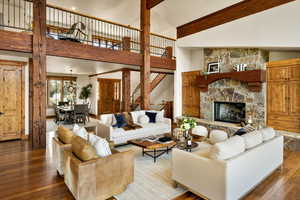 Living room with beam ceiling, high vaulted ceiling, a stone fireplace, hardwood / wood-style floors, and stairway