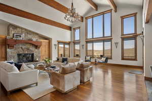 Living area featuring an inviting chandelier, beam ceiling, a stone fireplace, hardwood / wood-style floors, and baseboards