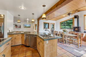 Kitchen with wood ceiling, a wood stove, a sink, stainless steel appliances, and light brown cabinetry