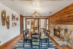 Dining room with rustic walls, a chandelier, a fireplace, tile patterned floors, and baseboards
