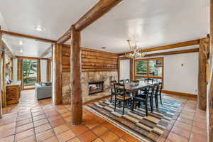 Dining space featuring beamed ceiling, log walls, a chandelier, baseboards, and a stone fireplace