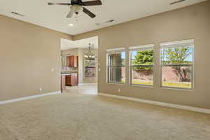 Unfurnished living room with baseboards, light colored carpet, visible vents, and ceiling fan with notable chandelier