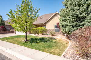 View of property hidden behind natural elements with stone siding, a garage, stucco siding, a front yard, and concrete driveway