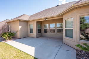 Back of property featuring a shingled roof, stucco siding, and a patio area