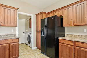 Kitchen featuring light countertops, separate washer and dryer, brown cabinets, and black refrigerator with ice dispenser
