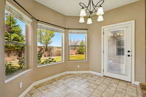 Unfurnished dining area featuring baseboards, stone tile flooring, and a notable chandelier