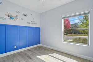 Spare room featuring wainscoting, ceiling fan, a decorative wall, and wood finished floors
