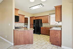 Kitchen with a peninsula, baseboards, light countertops, a sink, and black fridge
