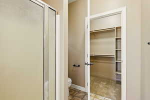 Bathroom with a walk in closet, baseboards, a stall shower, and toilet
