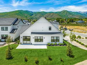 Back of property with a lawn, a mountain view, a shingled roof, and a patio area