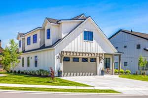 Modern inspired farmhouse featuring board and batten siding, a garage, a front lawn, concrete driveway, and a shingled roof