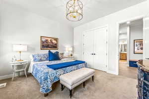 Carpeted bedroom with a notable chandelier, baseboards, ensuite bathroom, visible vents, and a closet