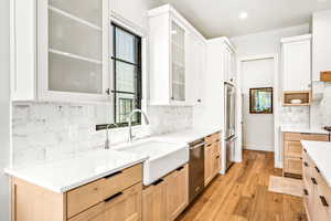 Kitchen featuring appliances with stainless steel finishes, tasteful backsplash, a sink, light countertops, and light wood-style flooring