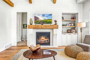 Living room featuring a glass covered fireplace, beamed ceiling, light wood-type flooring, and visible vents