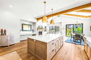 Kitchen with light countertops, lofted ceiling with beams, light wood finished floors, a warm lit fireplace, and recessed lighting