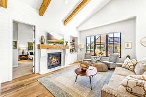 Living room featuring a glass covered fireplace, wood finished floors, beam ceiling, high vaulted ceiling, and built in shelves