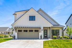 Modern farmhouse featuring board and batten siding, a standing seam roof, driveway, and a front yard
