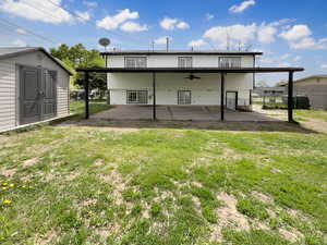 Rear view of house featuring ceiling fan, fence, a storage unit, a yard, and a patio