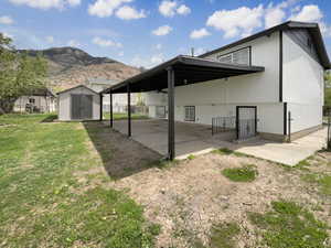 Back of property with a shed, a patio area, a lawn, a mountain view, and an outbuilding