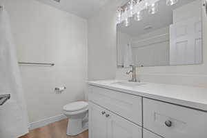 Bathroom featuring wood finished floors, toilet, vanity, baseboards, and visible vents