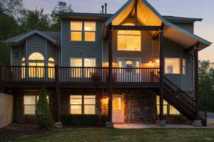 Rear view of property featuring a deck, stairs, and stone siding