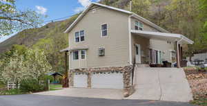 View of side of home with a garage, a mountain view, concrete driveway, and stone siding