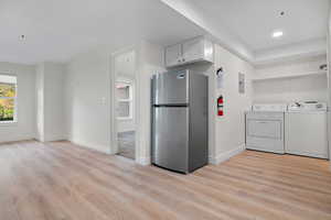 Kitchen with light wood finished floors, separate washer and dryer, electric panel, baseboards, and freestanding refrigerator