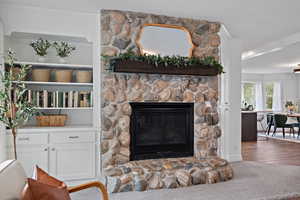 Living room with crown molding, a stone fireplace, and wood finished floors