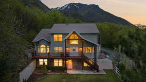 Back of house at dusk featuring stairs, stone siding, a patio area, a deck with mountain view, and a yard