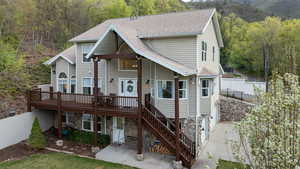 View of front of house featuring fence, a deck with mountain view, a forest view, and roof with shingles