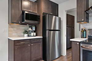 Kitchen featuring tasteful backsplash, stainless steel appliances, dark brown cabinets, light countertops, and dark wood-style flooring