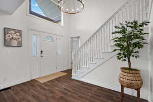 Foyer with dark wood-type flooring, a high ceiling, stairs, and baseboards