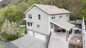 Rear view of property with stone siding, roof with shingles, concrete driveway, an attached garage, and fence