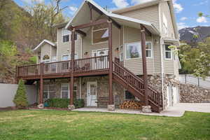 Back of house featuring concrete driveway, a lawn, stone siding, and a deck with mountain view