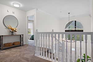 Hall with ornamental molding, a wealth of natural light, carpet floors, and an upstairs landing