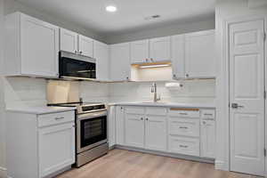 Kitchen featuring visible vents, appliances with stainless steel finishes, light countertops, and a sink