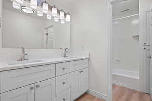 Full bath with double vanity, a sink, wood finished floors, and visible vents