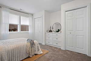 Carpeted bedroom featuring two closets, baseboards, and visible vents